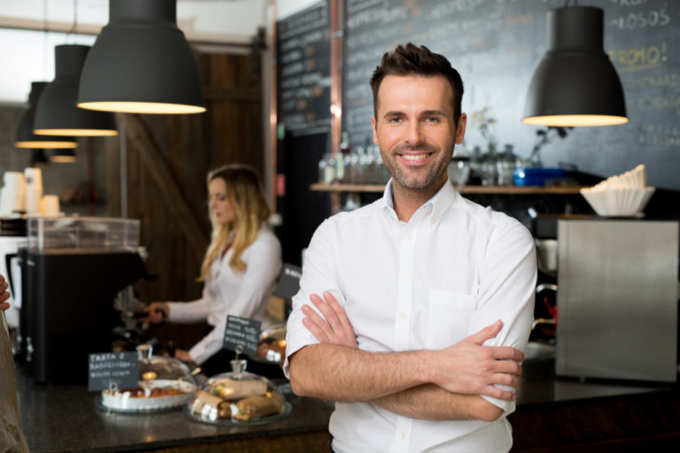 Businessowner with employee behind him making coffee