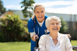 a female home care provider holding a senior woman's wheelchair while outdoors