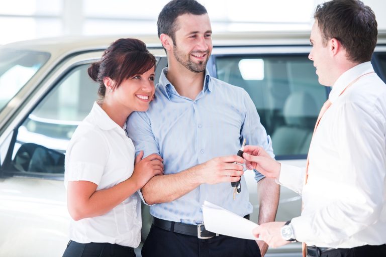 smiling couple buying a new car from a salesman